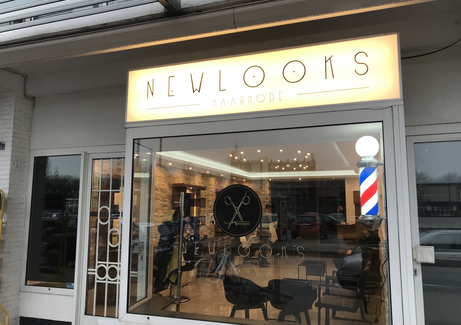 De winkel van Haarmode New Looks aan de Oude Wal bij avond: het verlichte NEWLOOKS-bord, de kapperspaal en de zaak achter het raam