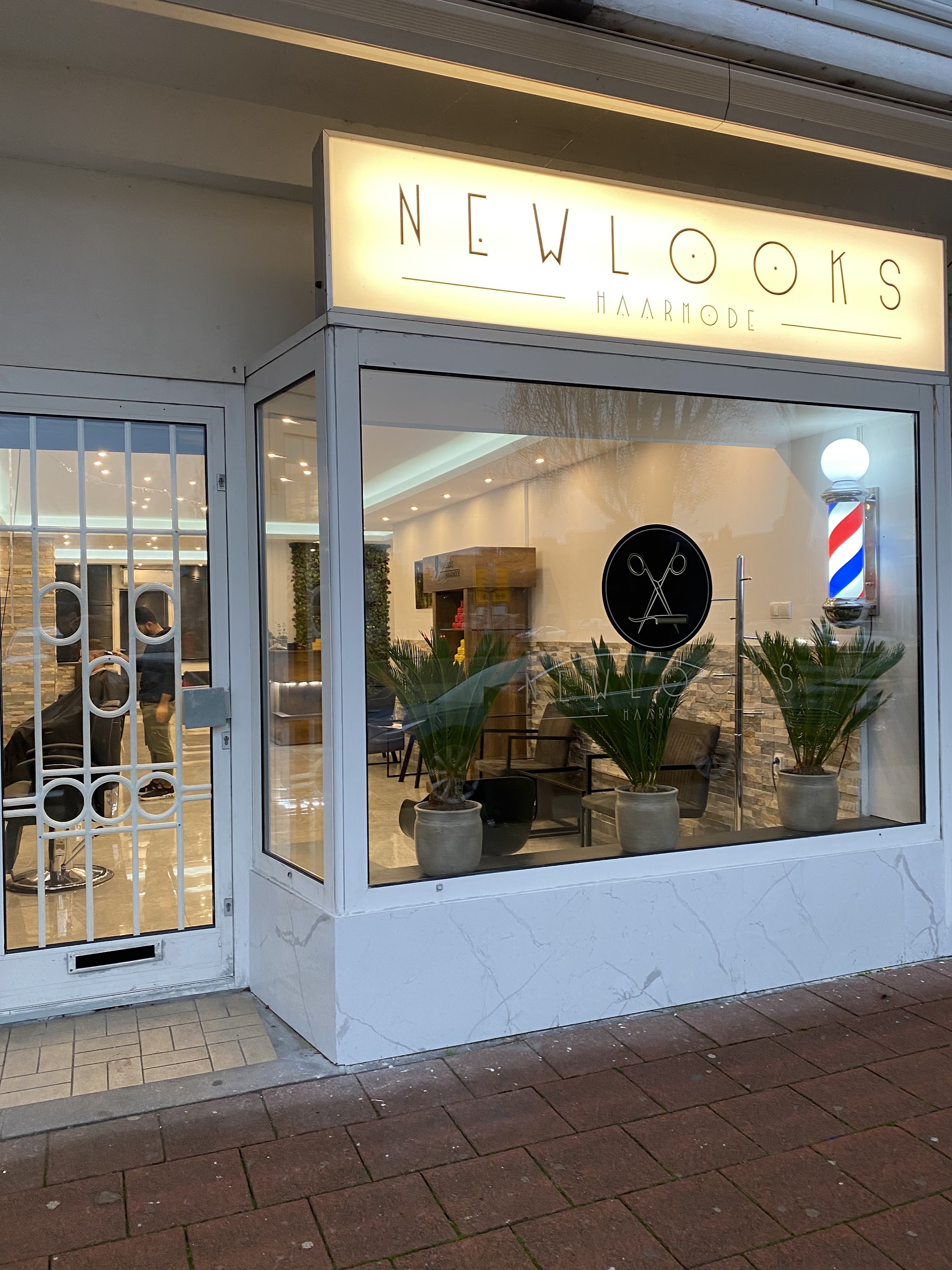 De voorkant van Haarmode New Looks overdag, met het NEWLOOKS-bord boven het raam en de kapperspaal